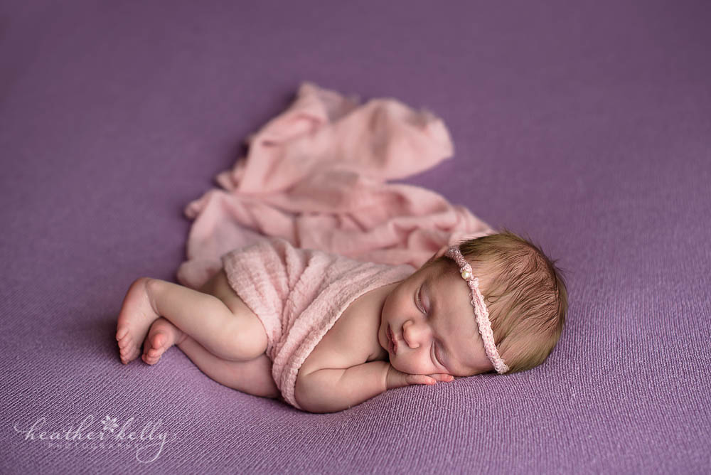 newborn girl with pink wrap and lavender blanket
