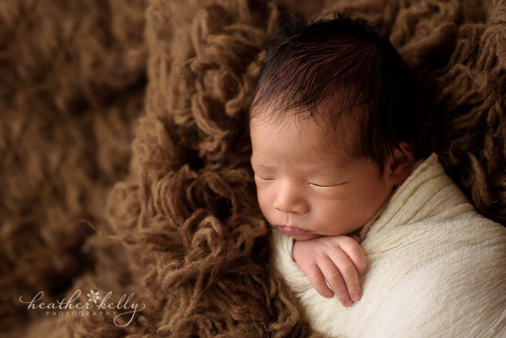 newborn on brown rug with tan wrap and little fingers sticking out photo