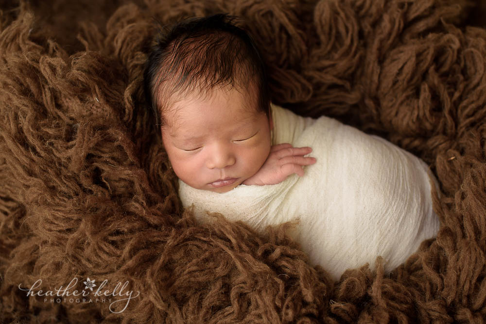 newborn boy wrapped in cream on brown flokati photo