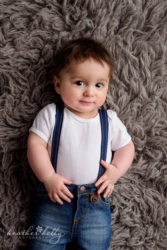adorable baby boy on gray rug wearing suspenders photo monroe baby photos ct photographer