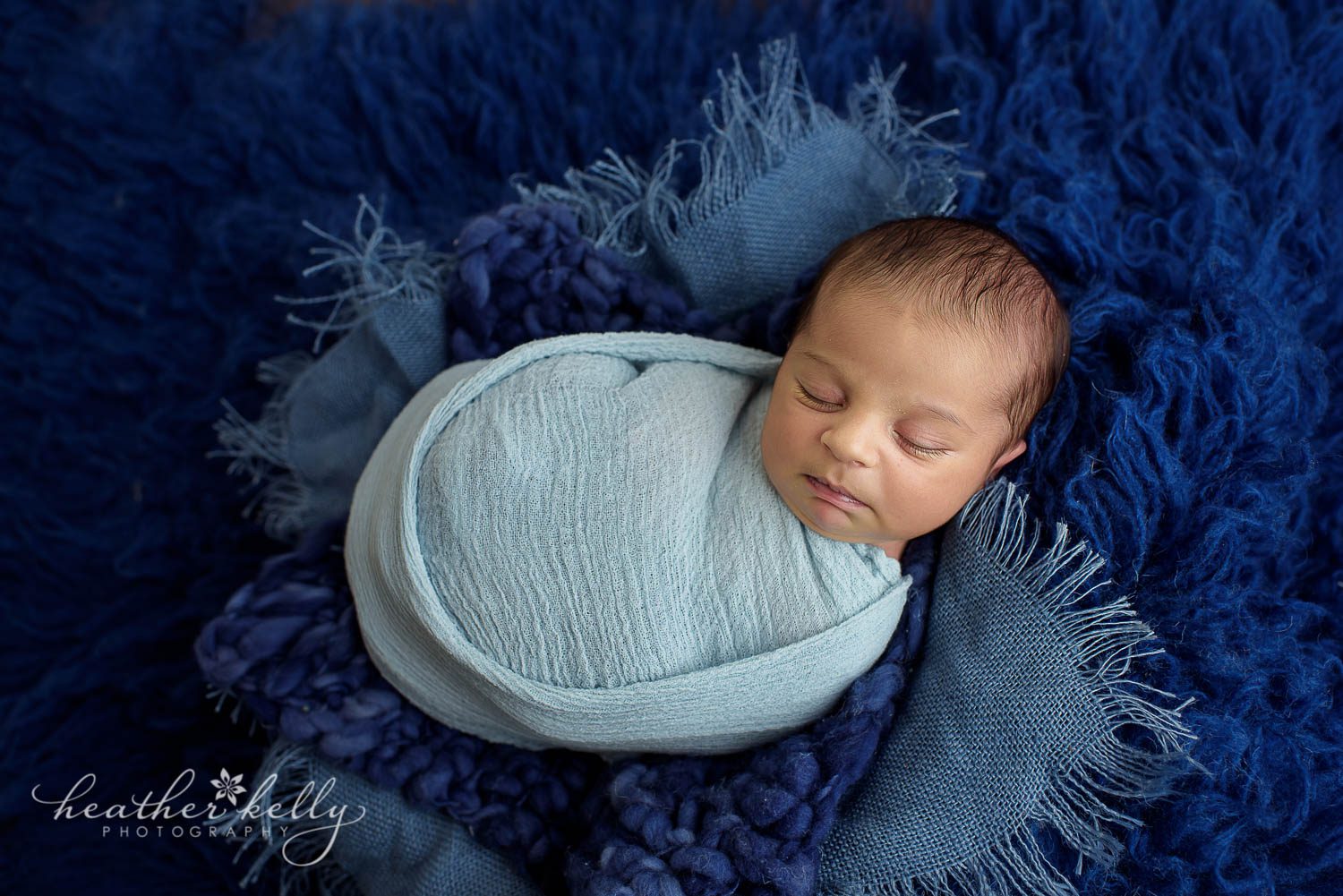 newborn photography. Baby boy wrapped in light blue on dark blue rug photo. 