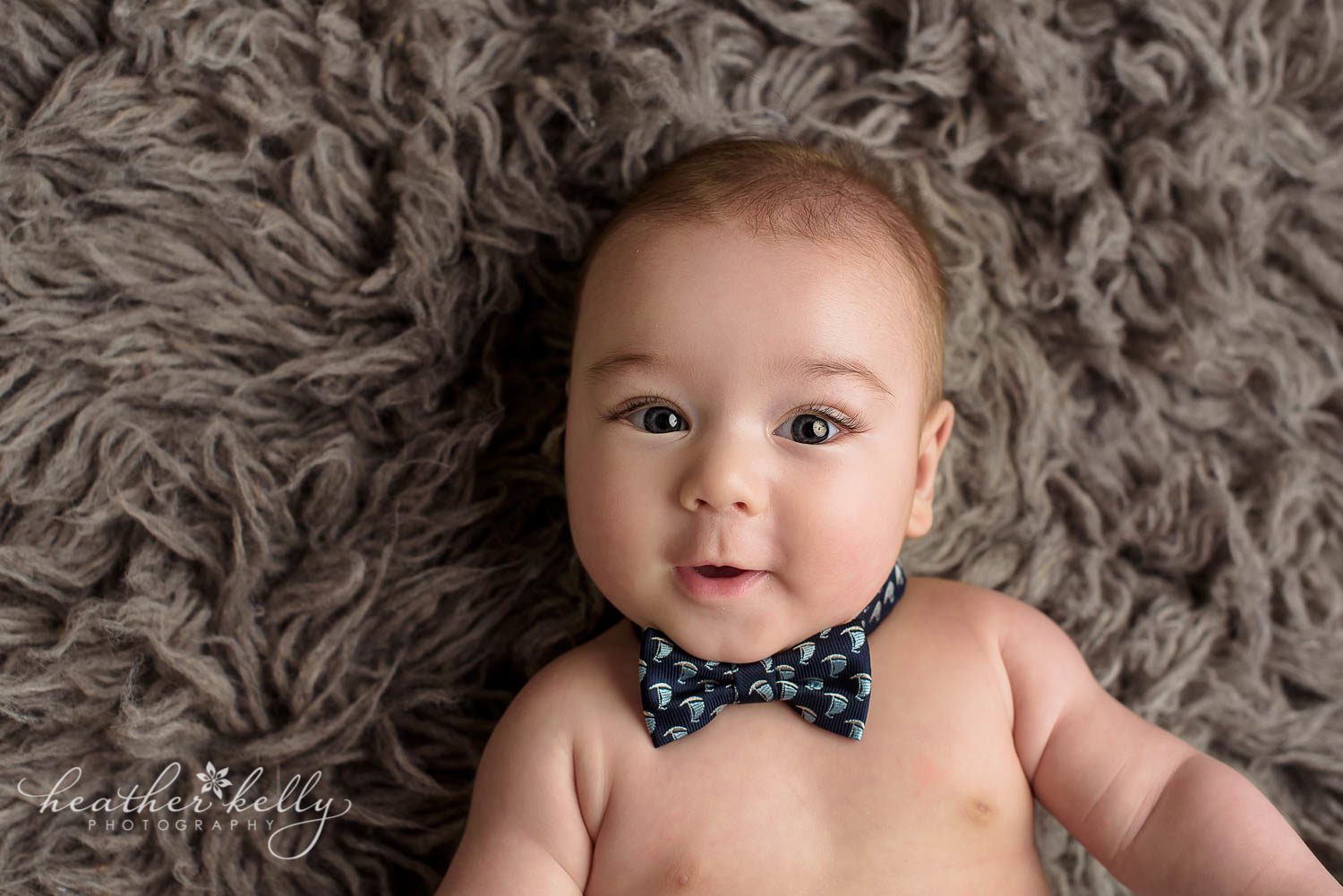 close up photo of 4 month baby boys face. He's wearing a bow tie on gray rug. sandy hook ct baby photography