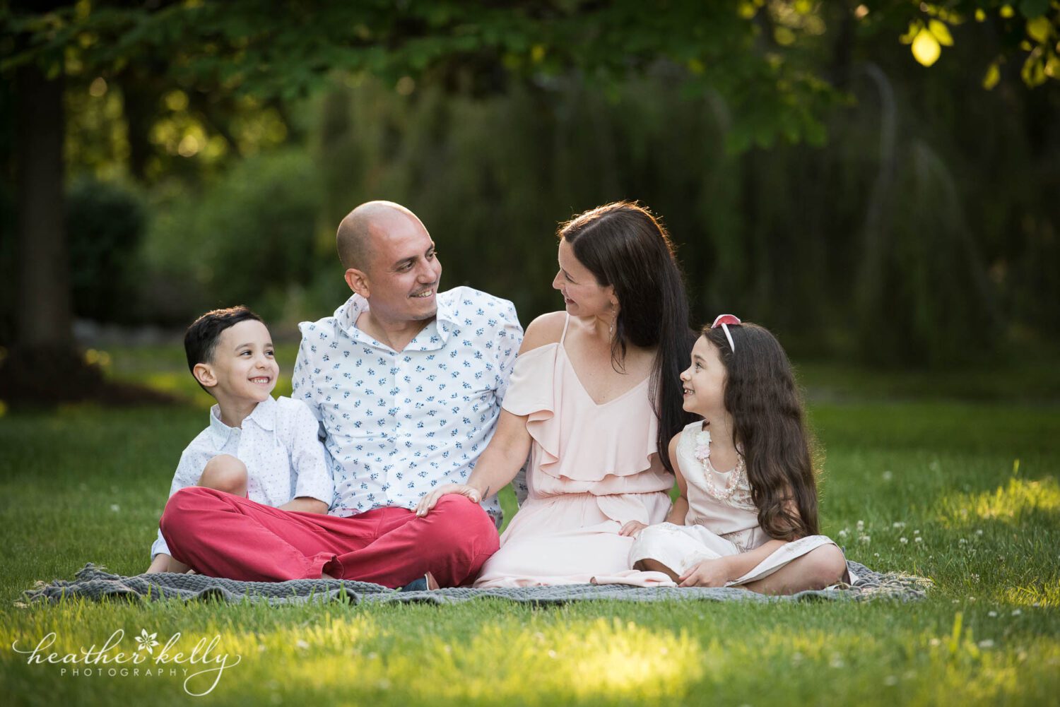 a family of four looking at each other while sitting in the grass at their monroe ct family photography session. 