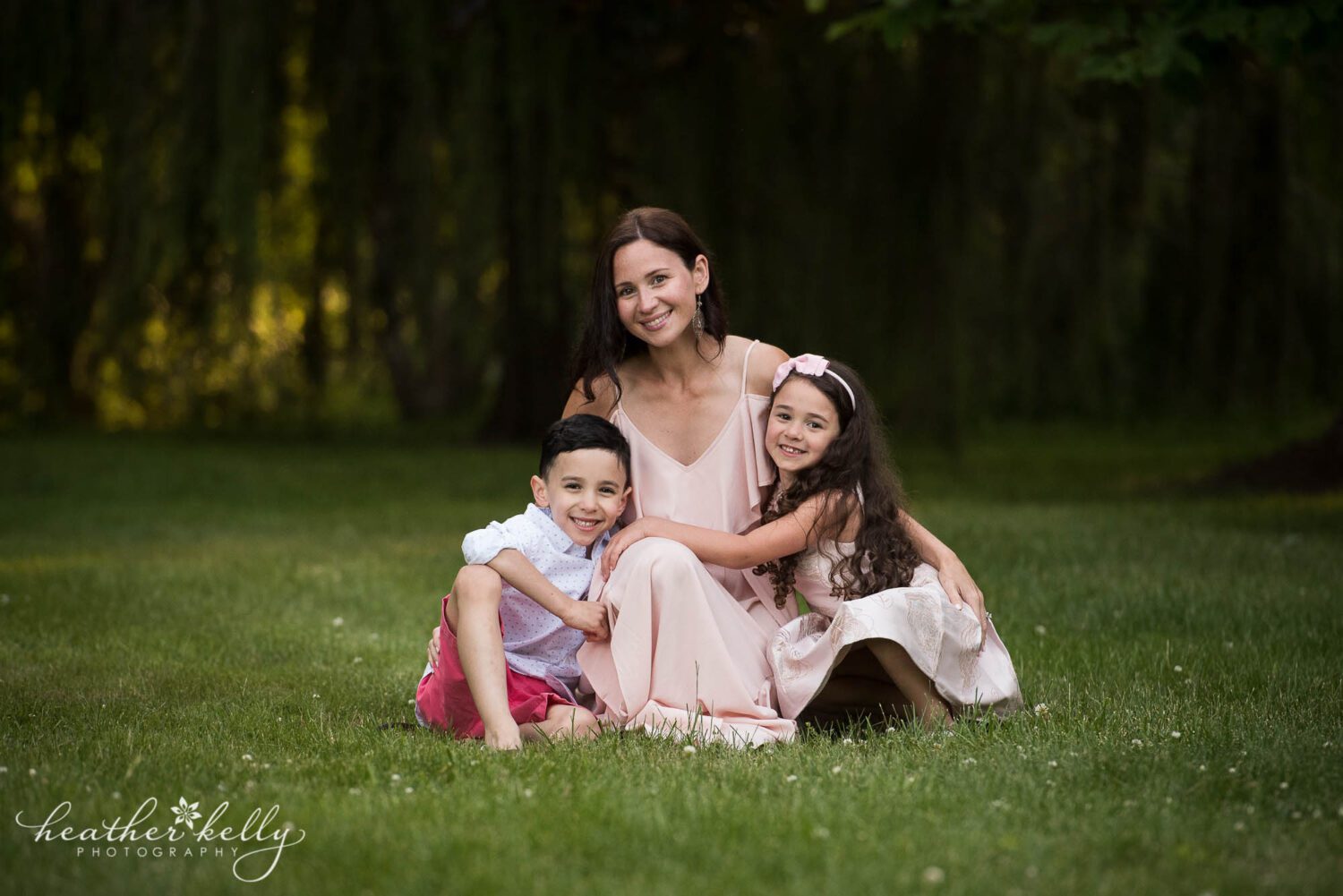 mom and her son and daughter cuddle together on the lush green grass during their monroe ct family photography session