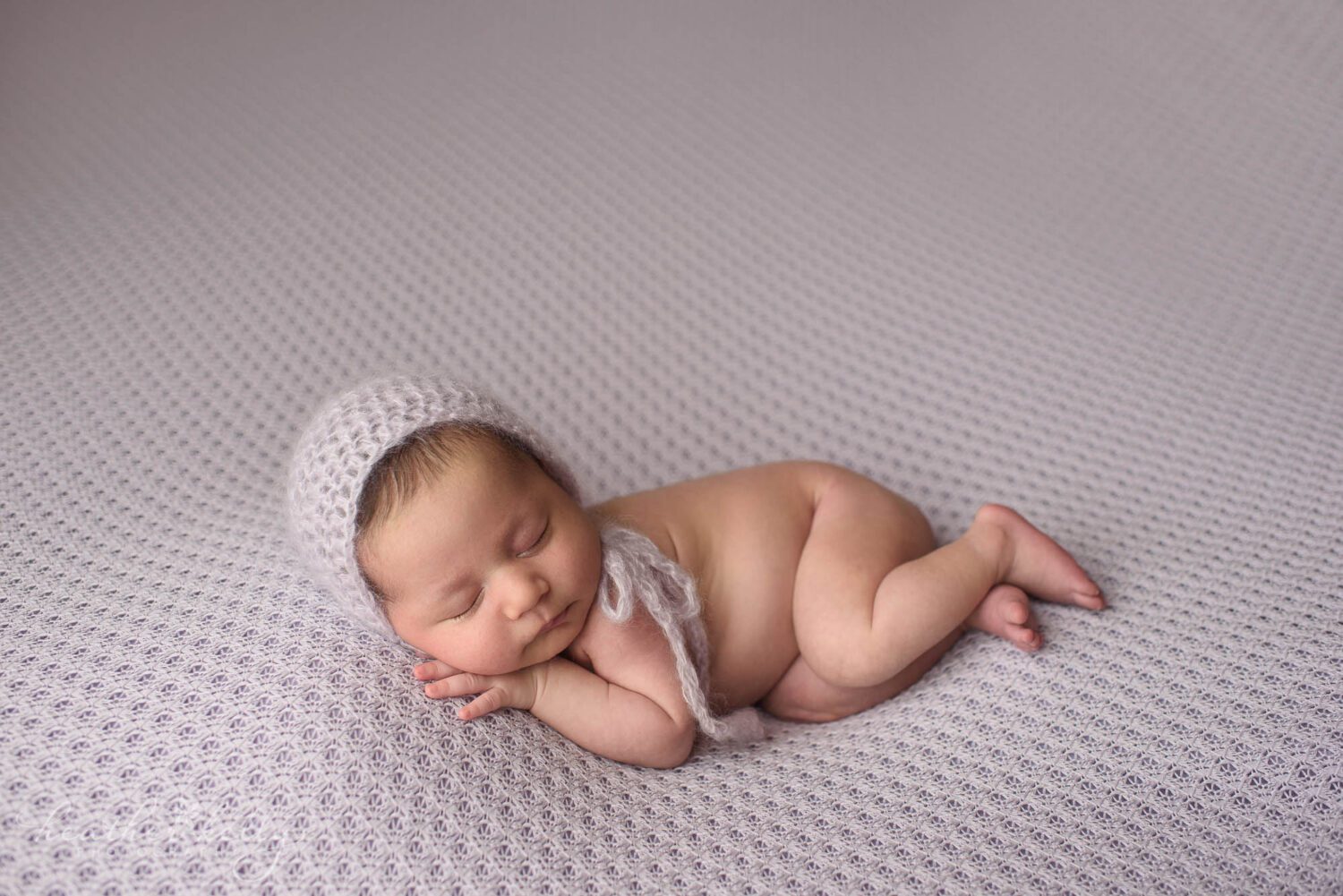 A newborn girl sleeping on a pale purple backdrop with a purple knit hat. Newborn photography