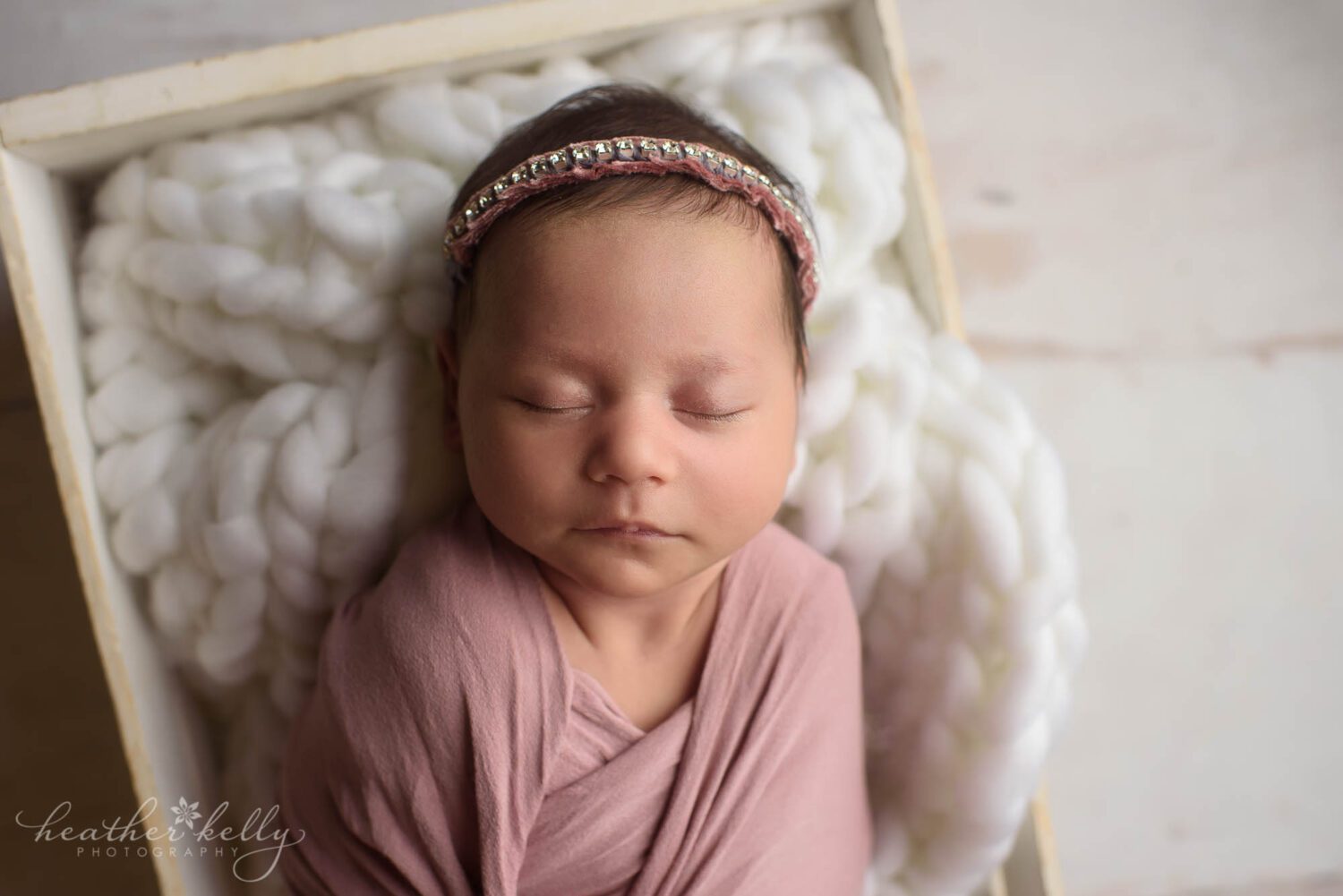 newborn photo of a baby girl wrapped in pink, sleeping in a white crate