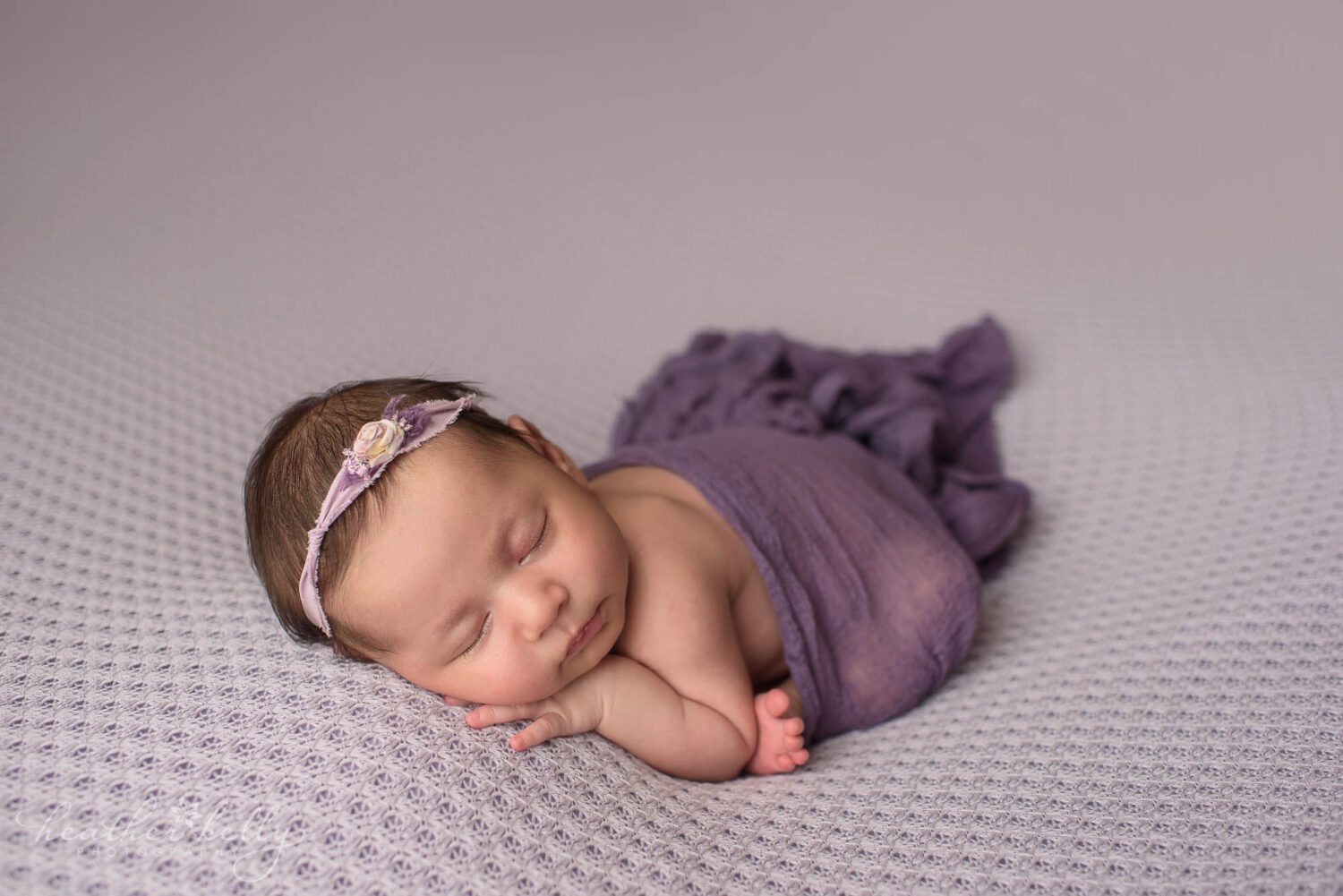 newborn photography image sleeping newborn girl on purple backdrop with a purple wrap around her bottom