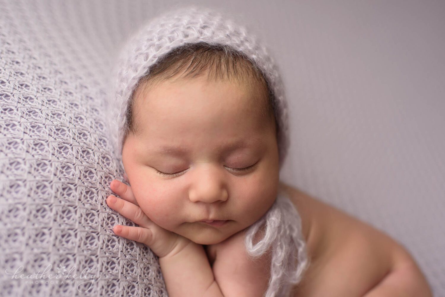newborn photography close up image of a newborn girl sleeping. She has a purple knit bonnet on her head. 