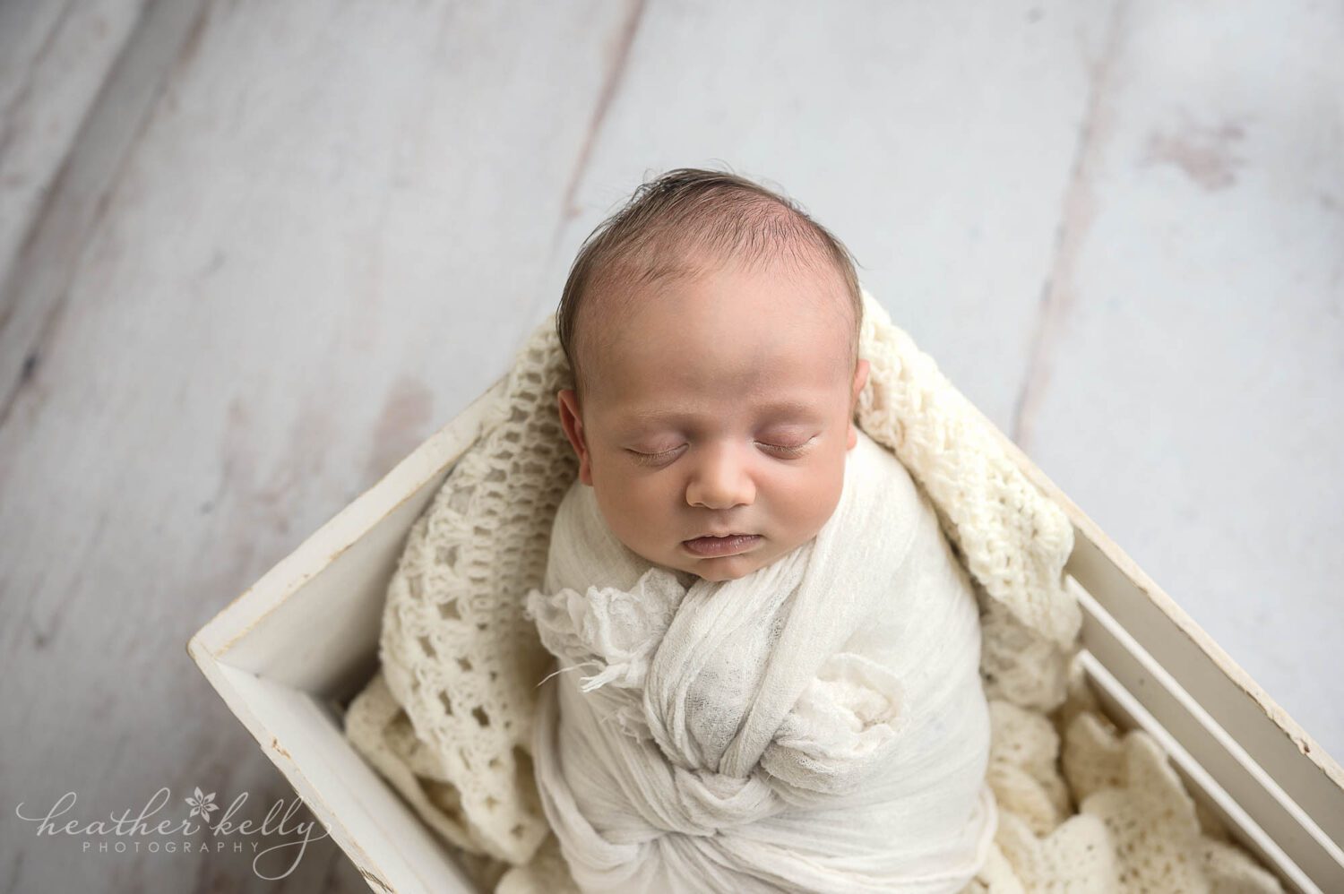 Newborn boy is wrapped in white and is posed carefully in a white box crate with a white wood floor. ct newborn