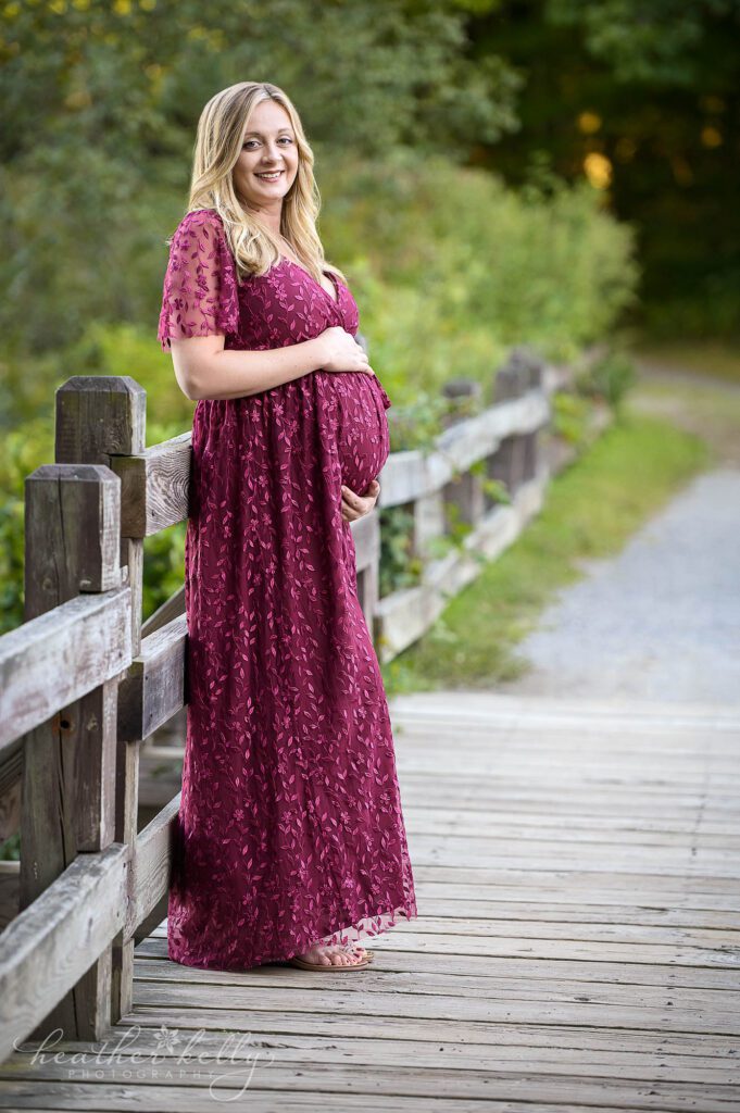 A pregnant mom to be leans against a fence with her arms wrapped around her belly. Located in Southbury CT. 
