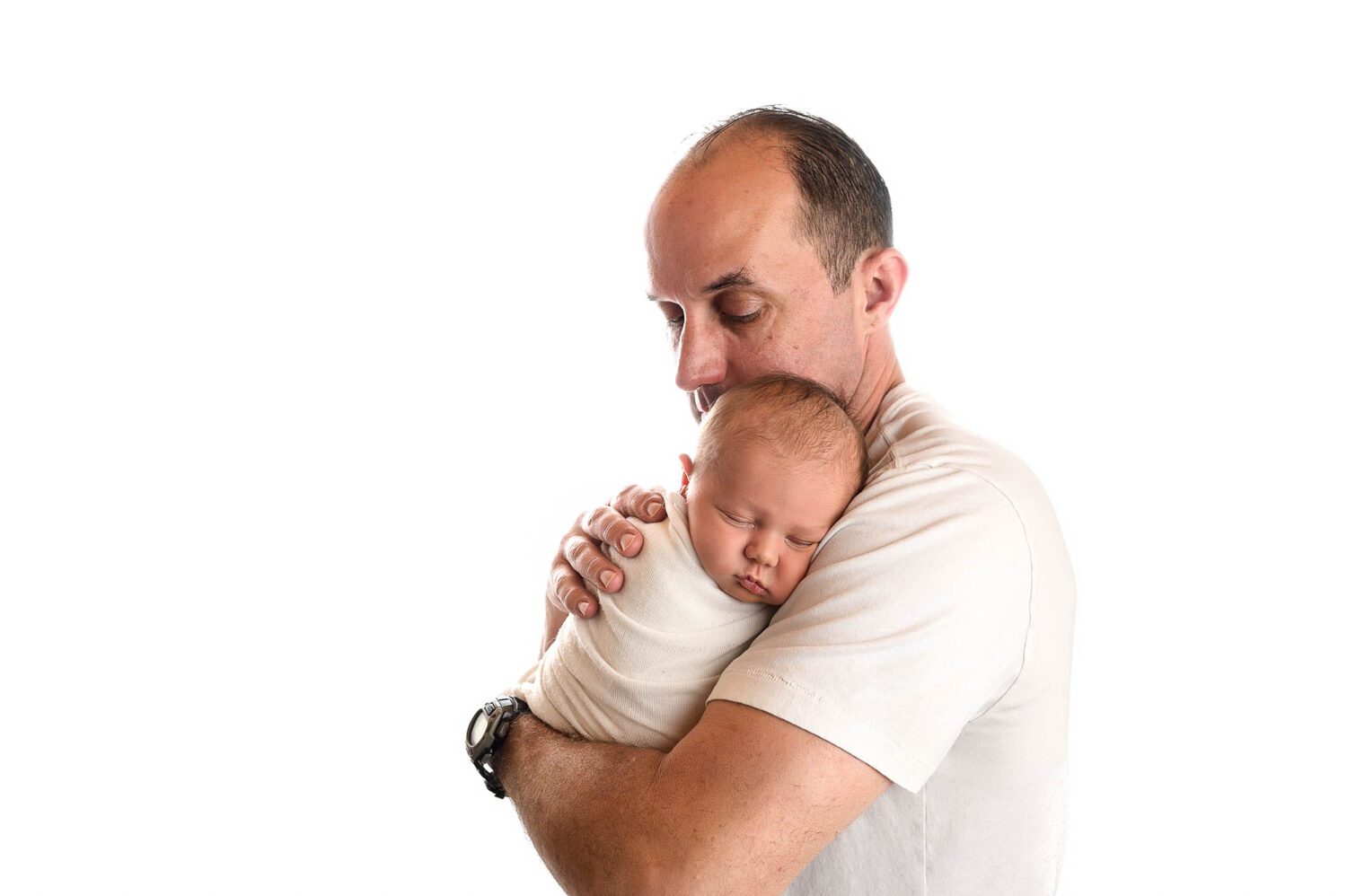 A dad holds his newborn boy on his shoulder as he looks down at him. 