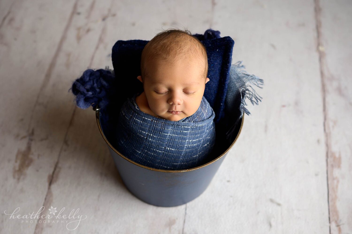 A newborn boy is posed in a bucket. 