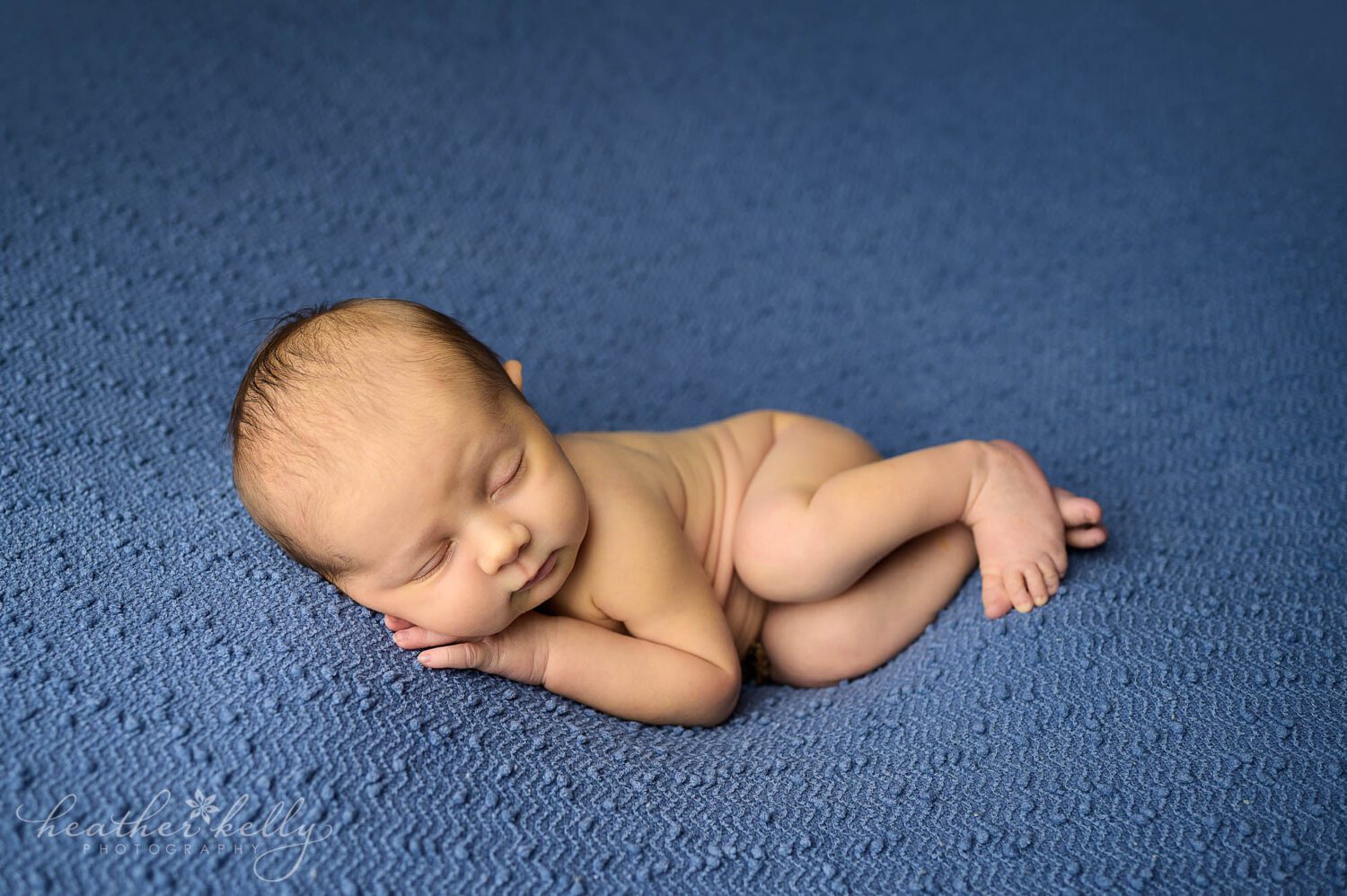 a newborn boy is posed on a blue blanket. He is sleeping 