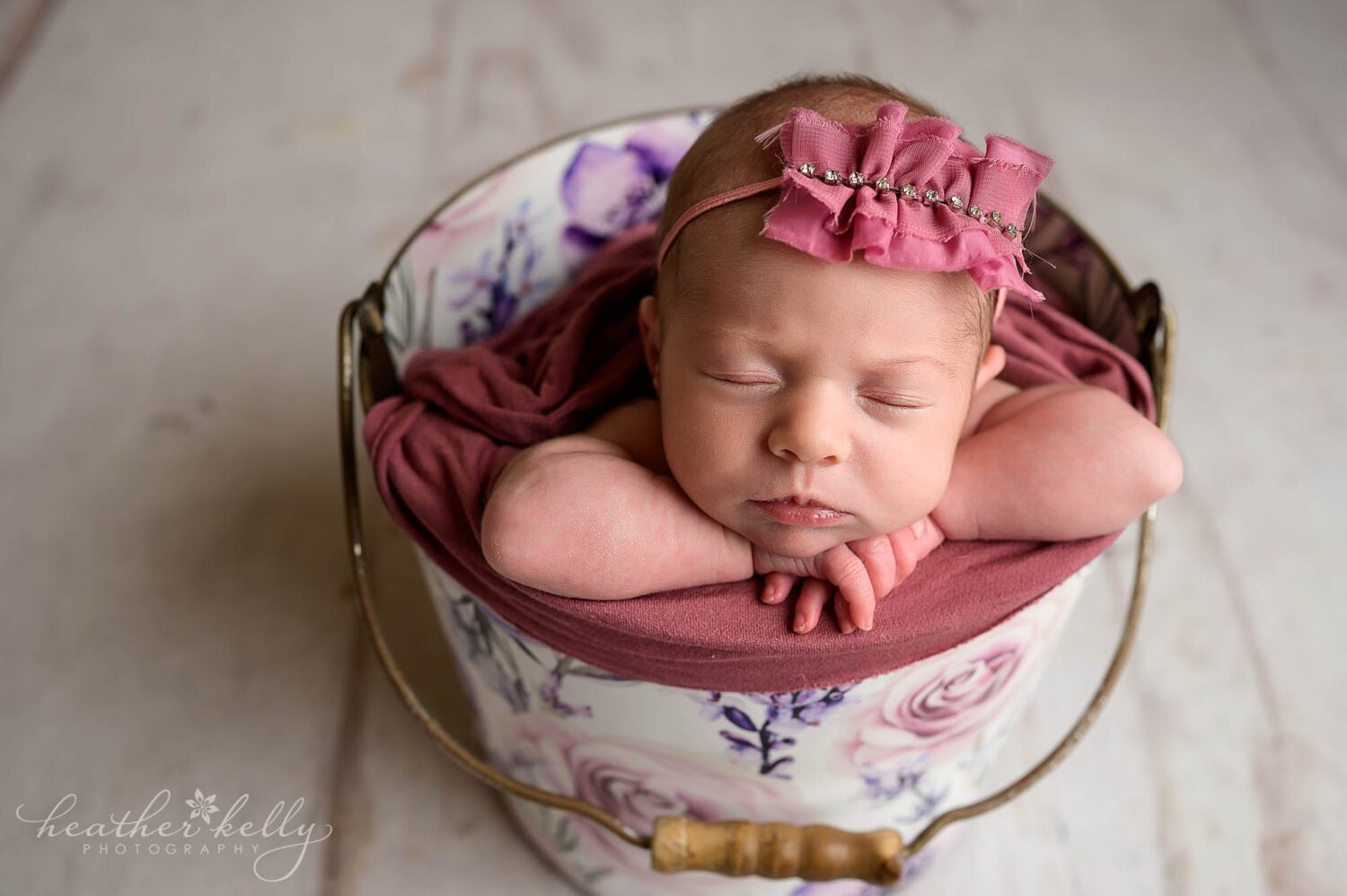 A newborn girl is in a bucket that has pink and purple flowers on it. 