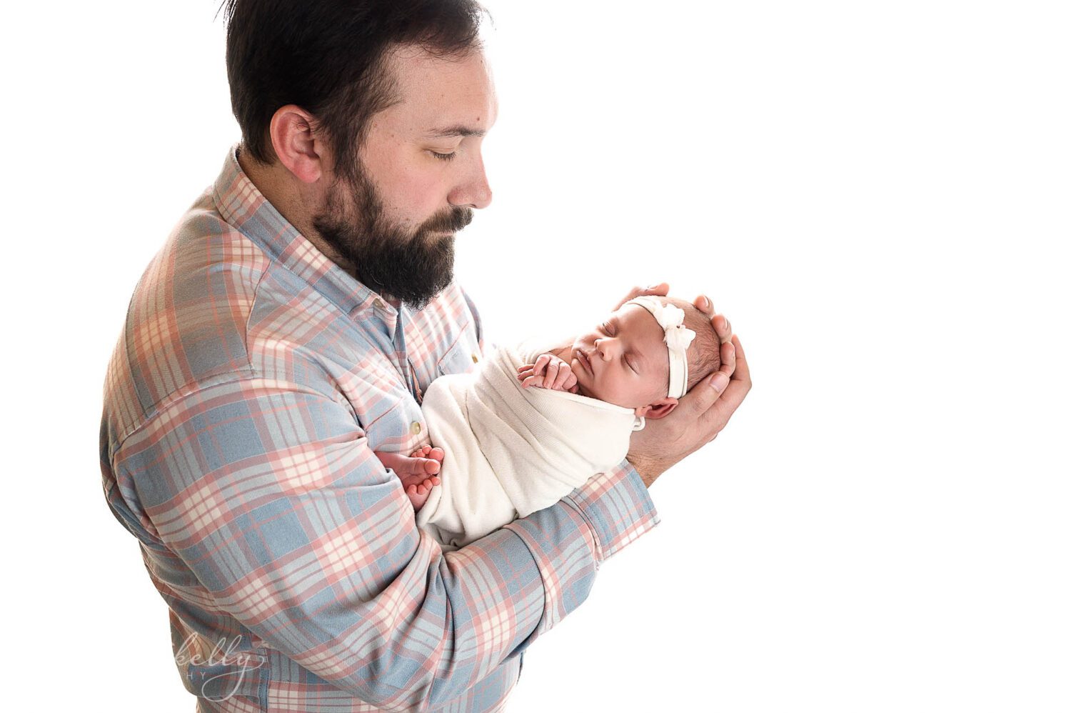 A dad holding and looking at his newborn baby girl. There's a white blown out background. 