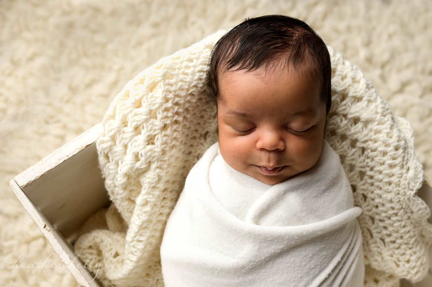 During a newborn photography session in Newtown CT, a baby boy is wrapped in a white swaddle and posed in a white crate. 