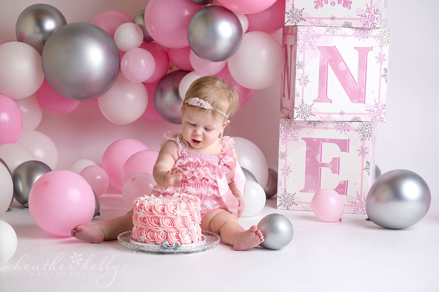a one year old girl in pink reaching out towards a cake to celebrate her first birthday in sandy hook ct. 