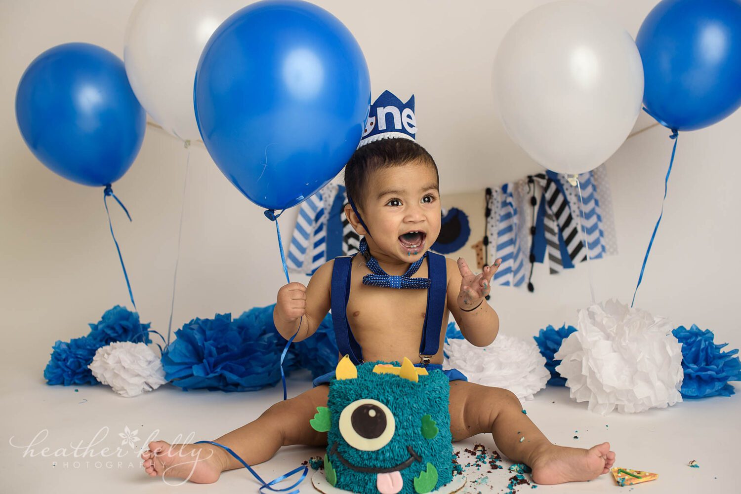 happy boy for his first birthday portrait cake smash session with a monster theme 