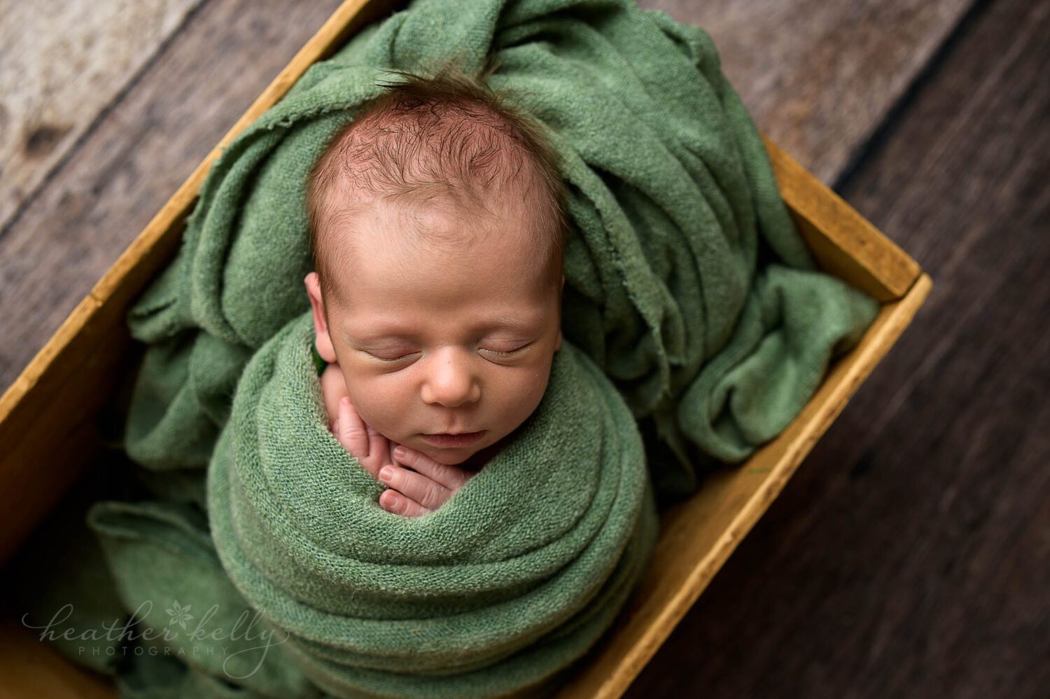 a baby boy is sleeping while wrapped in green and in a box 