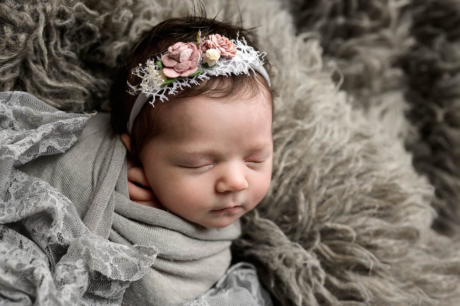 a newborn girl is wrapped in gray and sleeping on a gray flokati during her newborn session