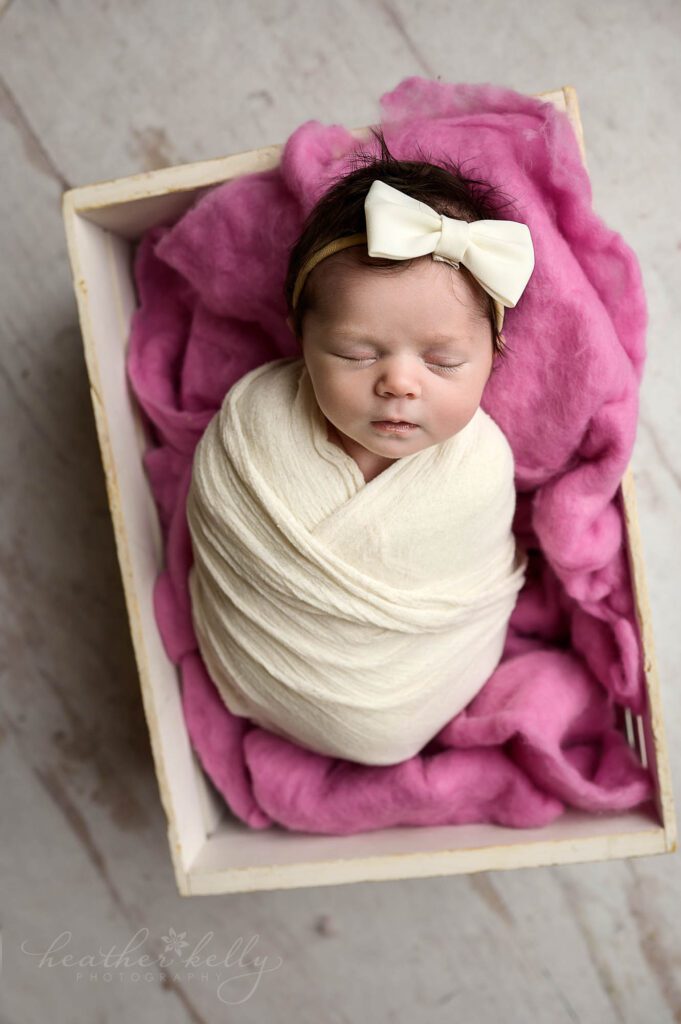 a CT newborn photographer captures an image of a baby girl sleeping in a white crate. 
