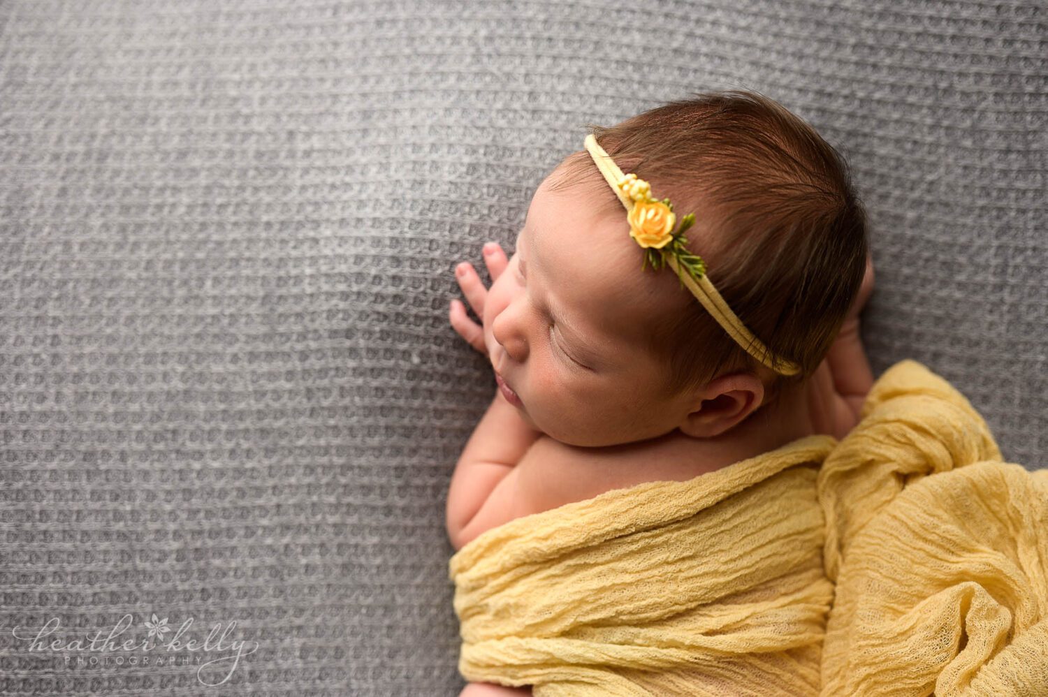 a profile picture of a sleepy newborn. She is draped in yellow and on a gray backdrop. 