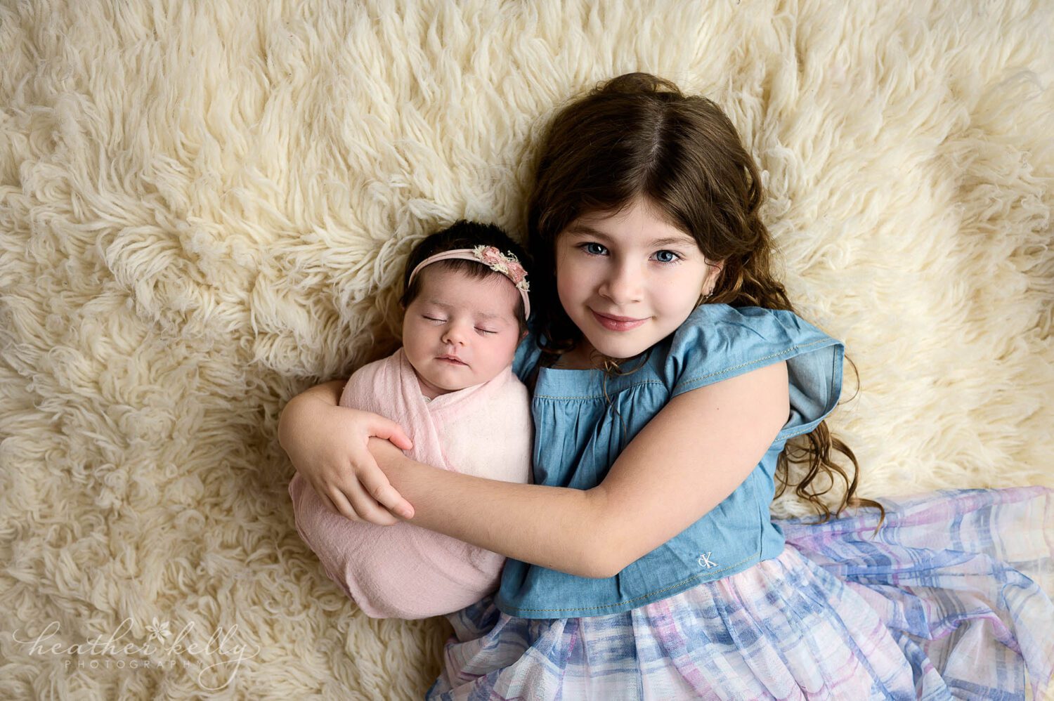 a sister holds her newborn sister who is swaddled in pink. 