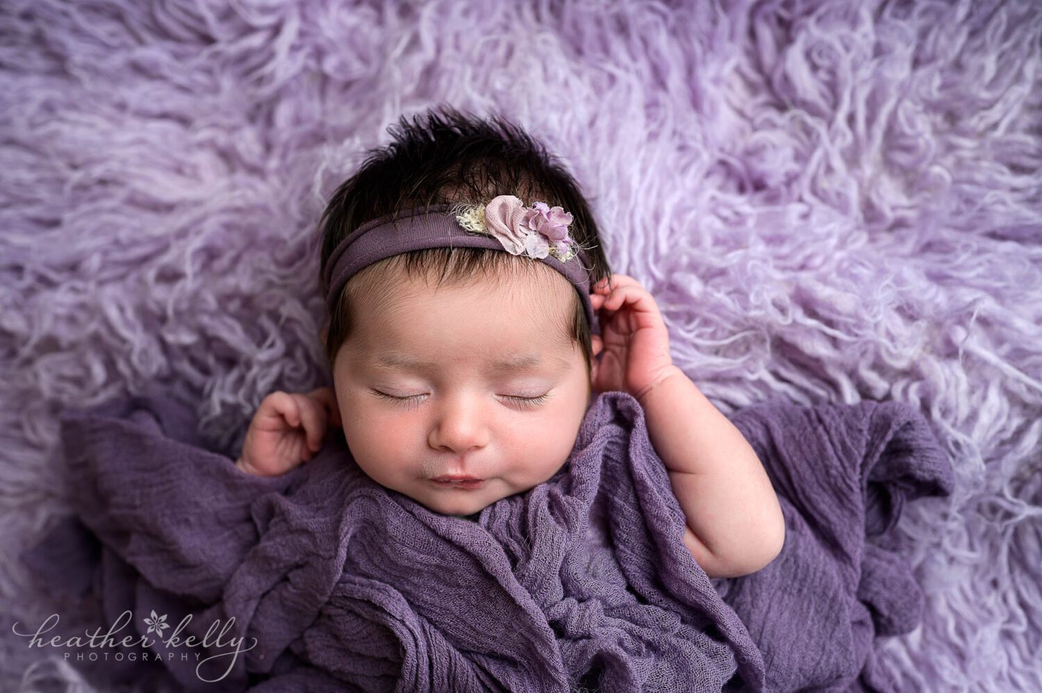a sleeping newborn in purple poses with her hands up by her head during her newtown ct newborn photography session. photos
