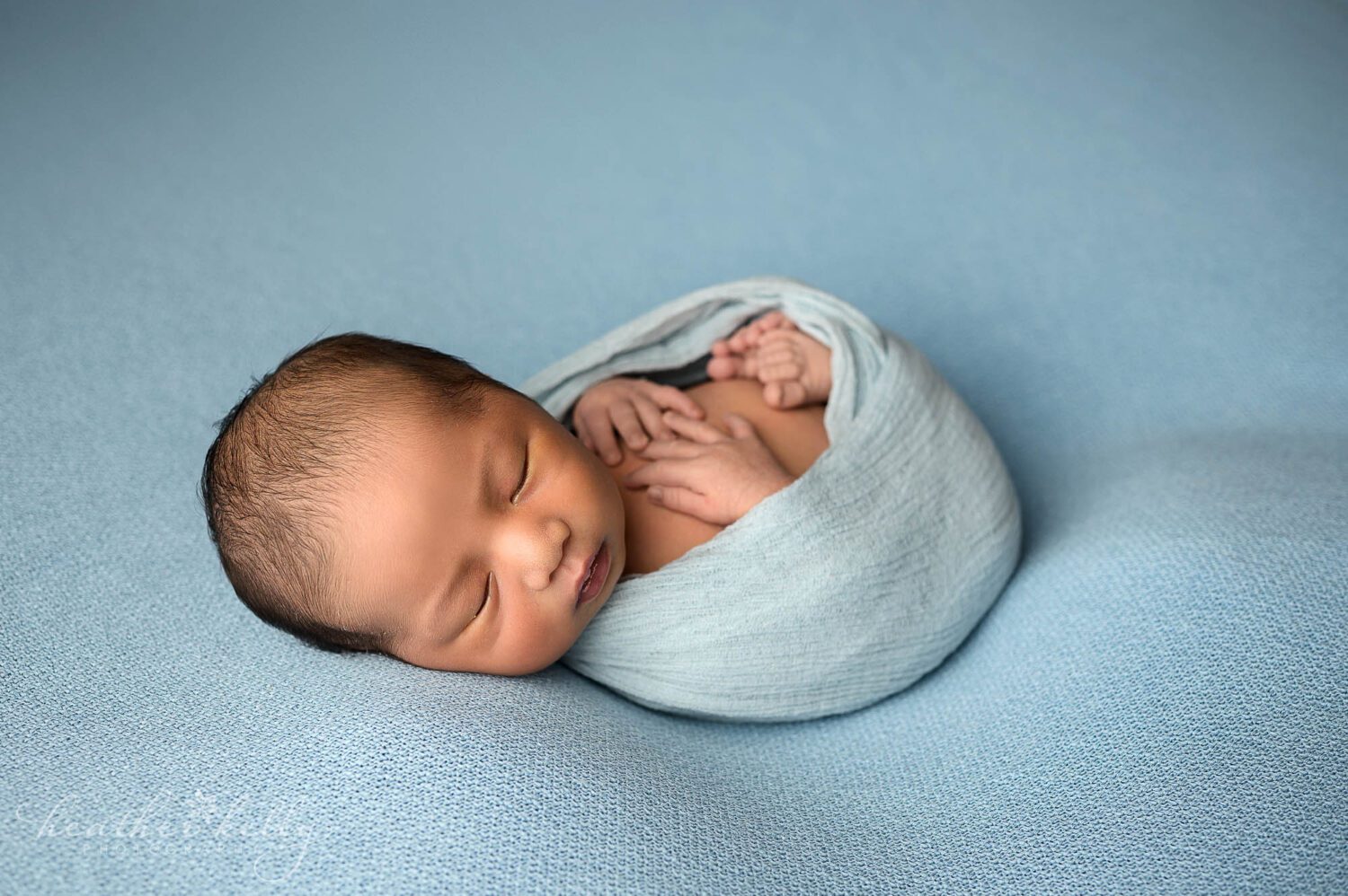 a newborn boy wrapped in blue with his hands and toes sticking out. 