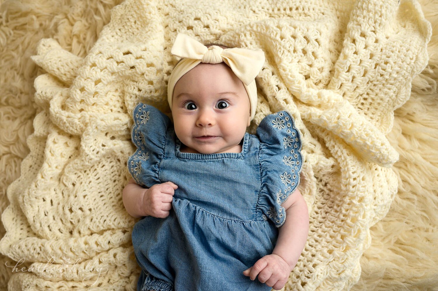 a 3 month old is laying on cream blankets. she is smiling and looking at the camera. 