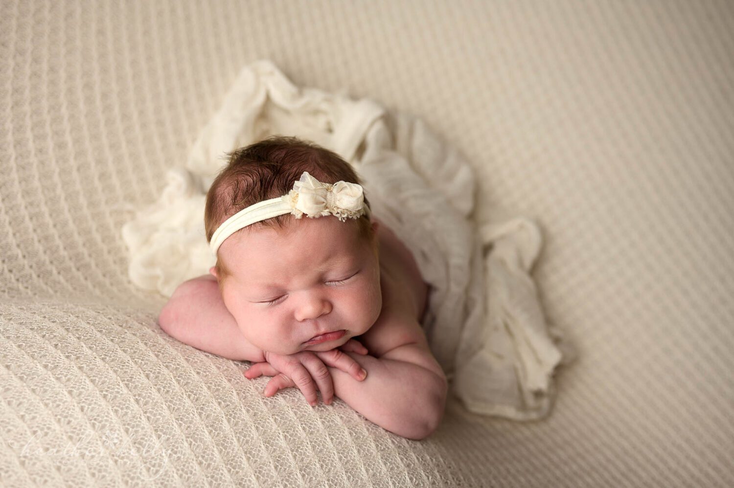 a newtown ct newborn session. A newborn girl lays on her hands with a white wrap draped over her. 