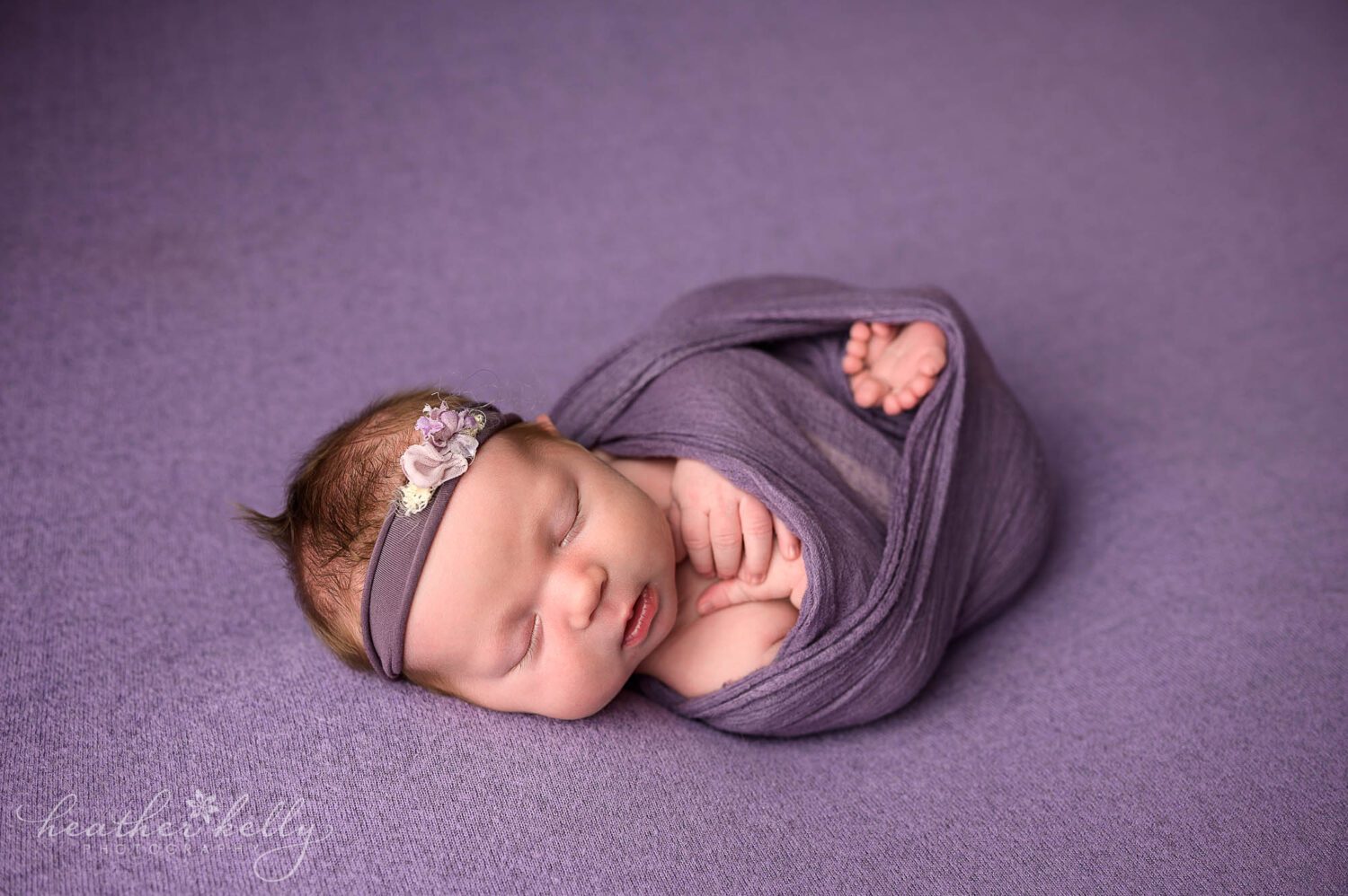 a newborn girl wrapped in purple sleeping 