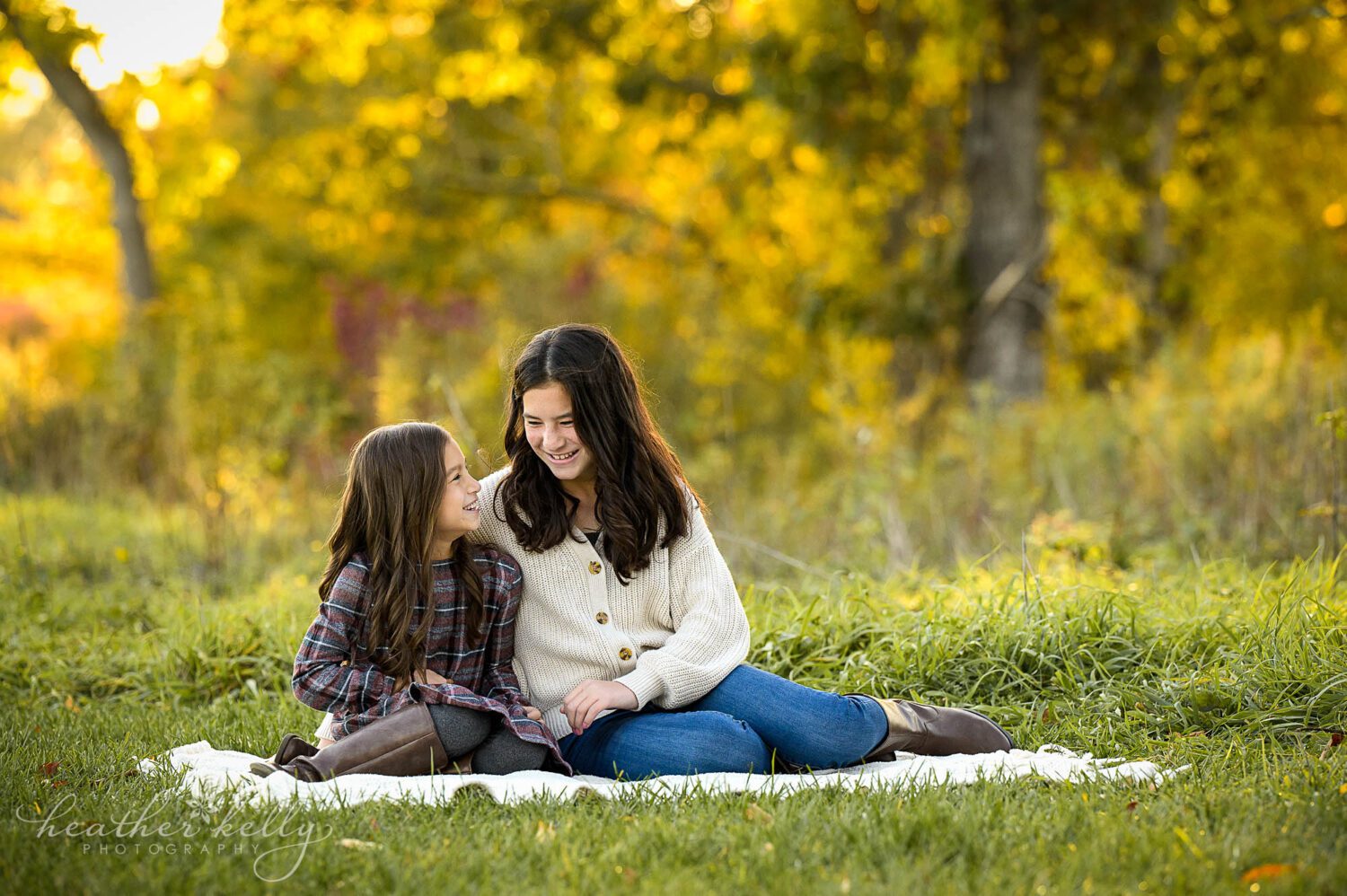 two sisters sit on a blanket and look at each other during a trumbull ct photography session